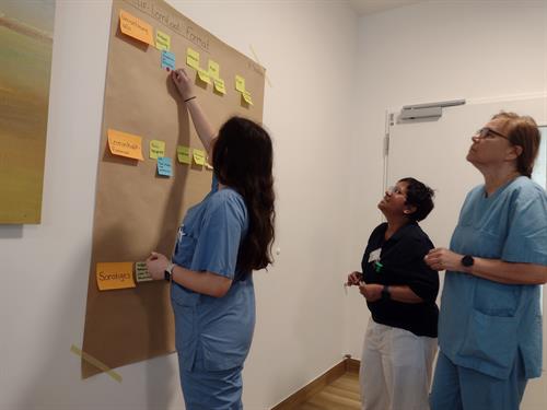 Workshop-Situation: Eine Frau mit langen Haaren klebt Markierungen auf ein Plakat an einer Wand.